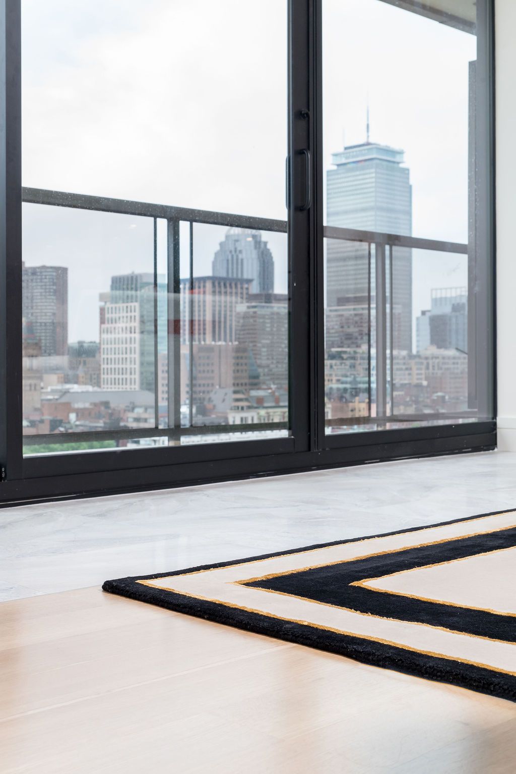 Modern apartment interior with large windows, city skyline view, and a striped rug on light wood floors