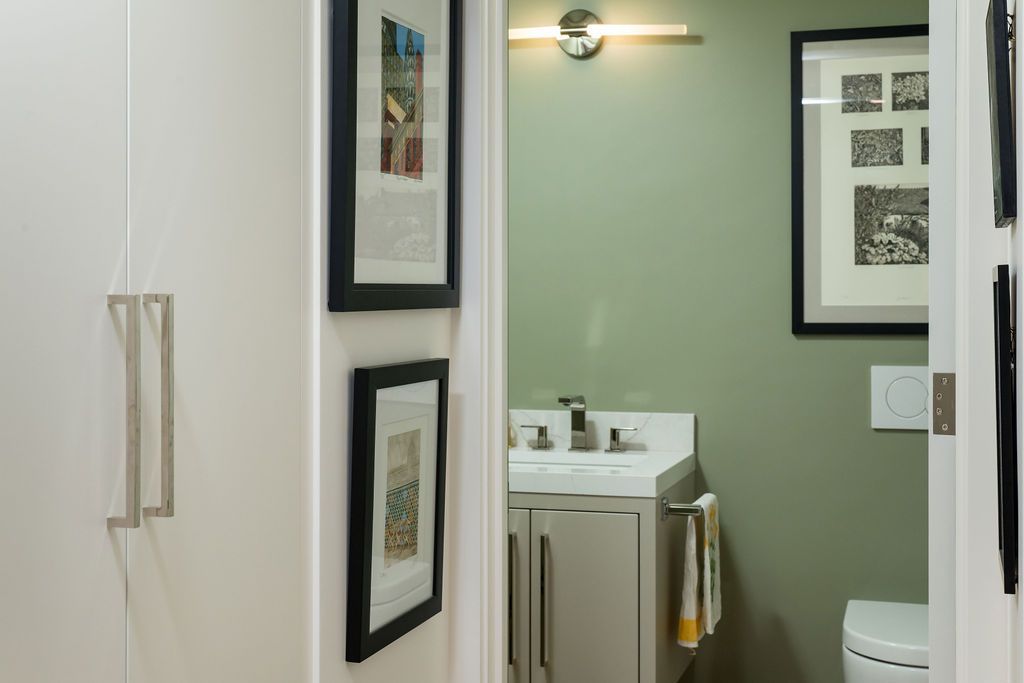 Bathroom vanity with green wall, mirror, framed art, and a partially visible toilet behind a sliding door.