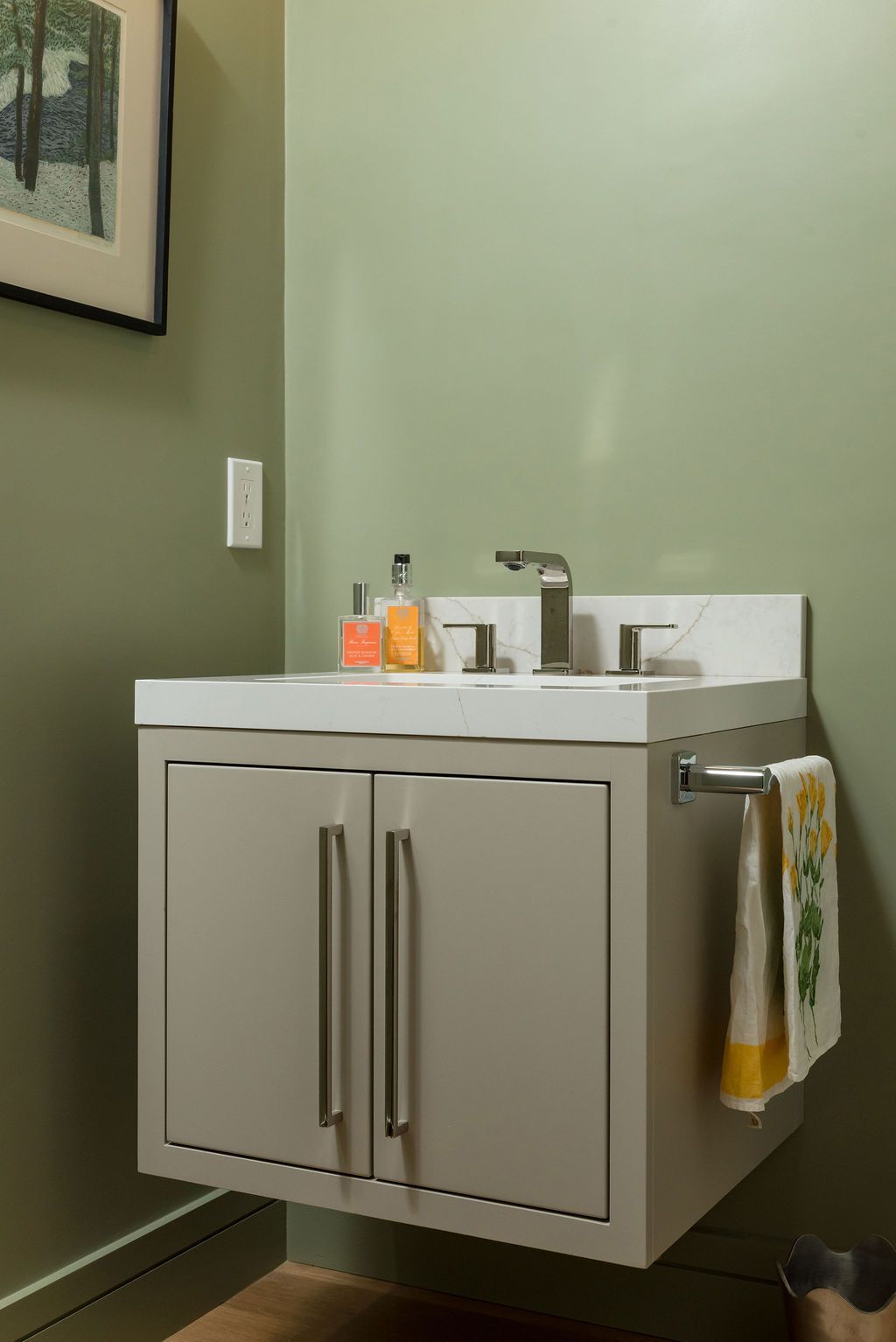 Small bathroom vanity with white sink, mirror, and towels against a pale green wall.