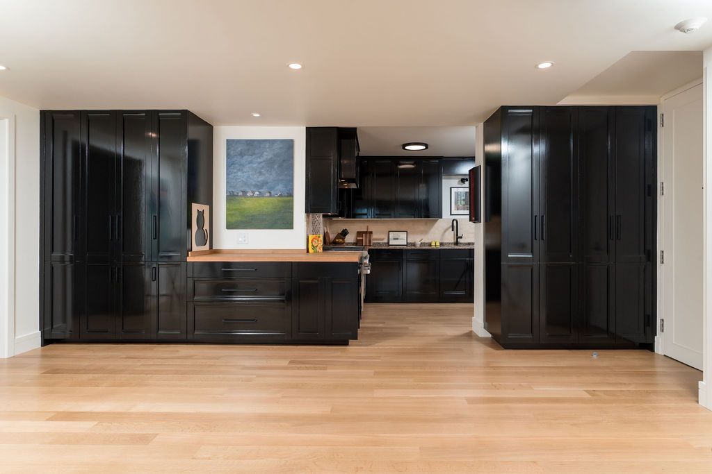 Modern open-plan kitchen with glossy black cabinets, wood floors, and a framed landscape painting.