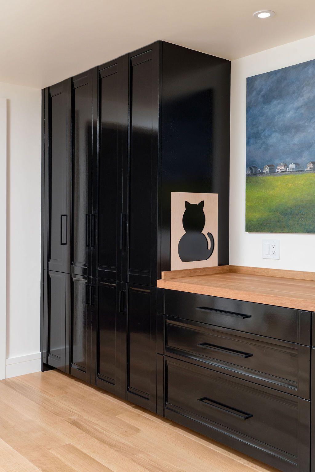 Black built-in cabinet and dresser with wood countertop in a modern room, with a cat silhouette print on top