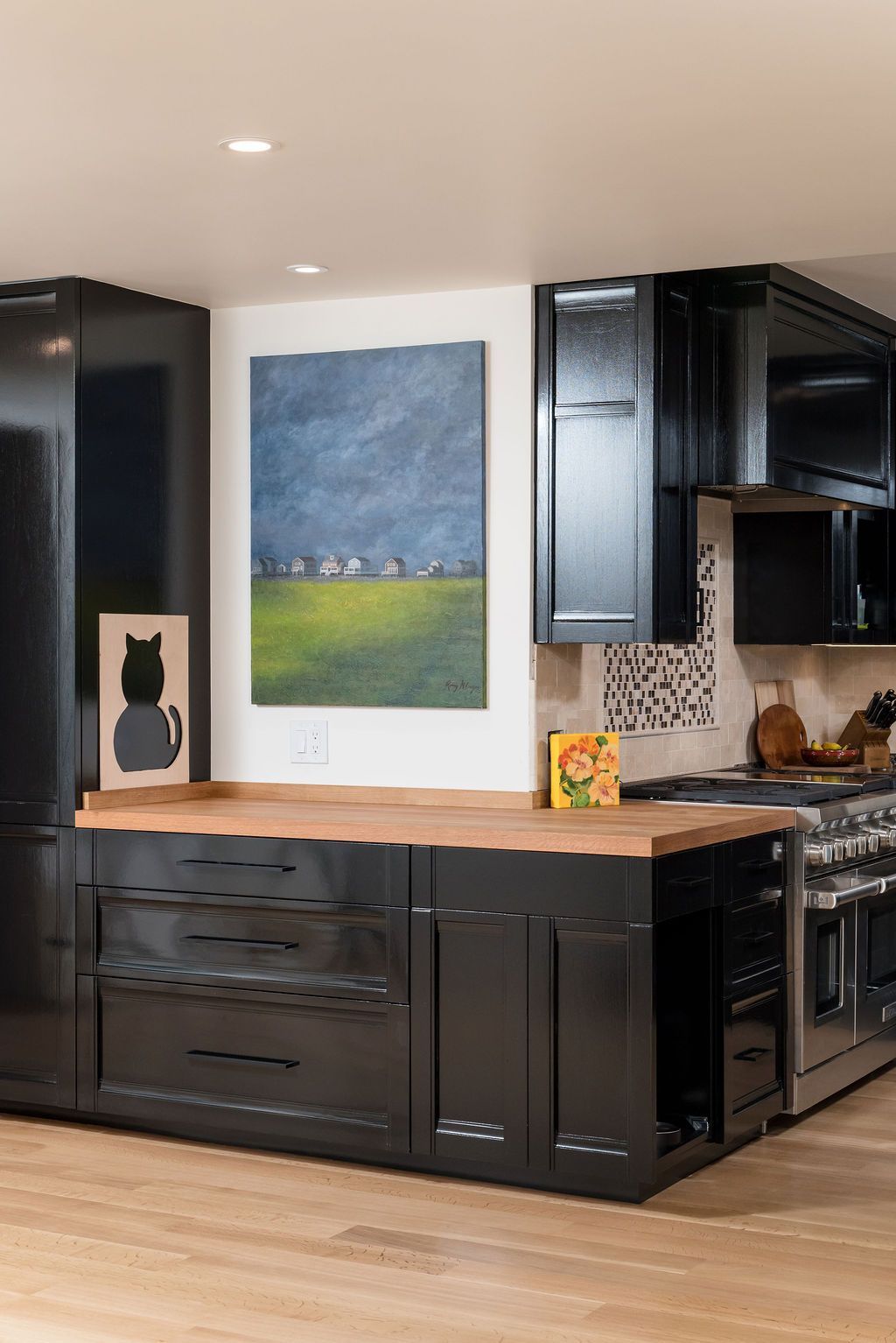 Modern kitchen with black cabinets, wood floor, marble island, and abstract wall art