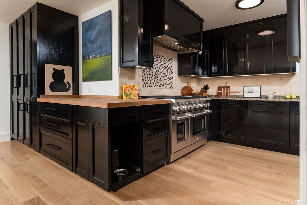 Modern black kitchen with island, stainless stove, dark cabinets, wood floors, and a colorful wall painting