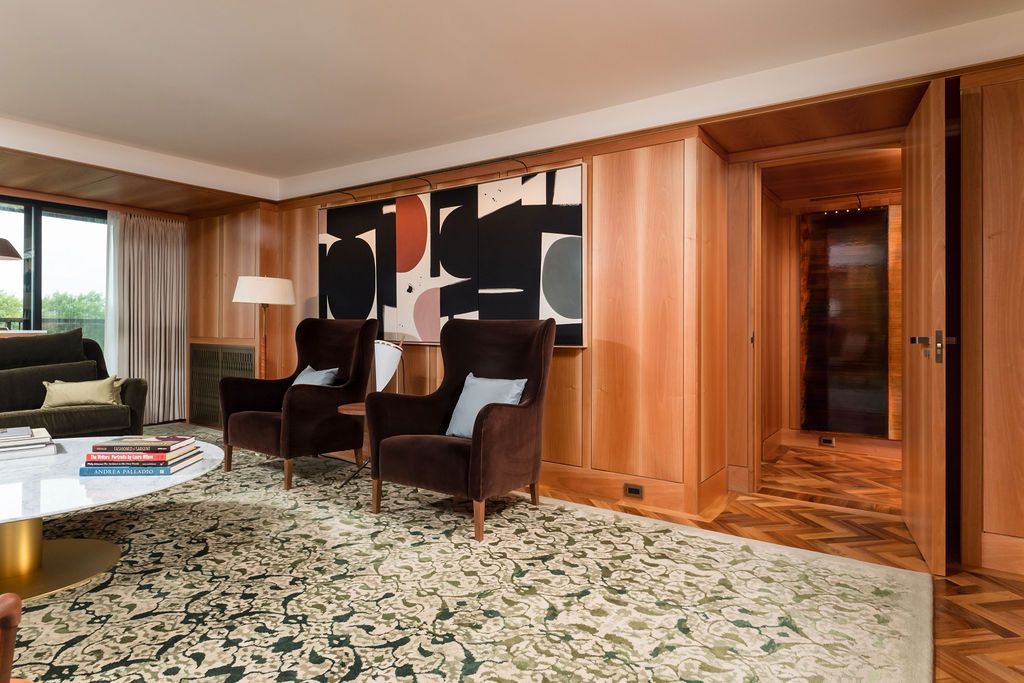 Spacious wood-paneled living room with patterned carpet, armchairs, and abstract wall art