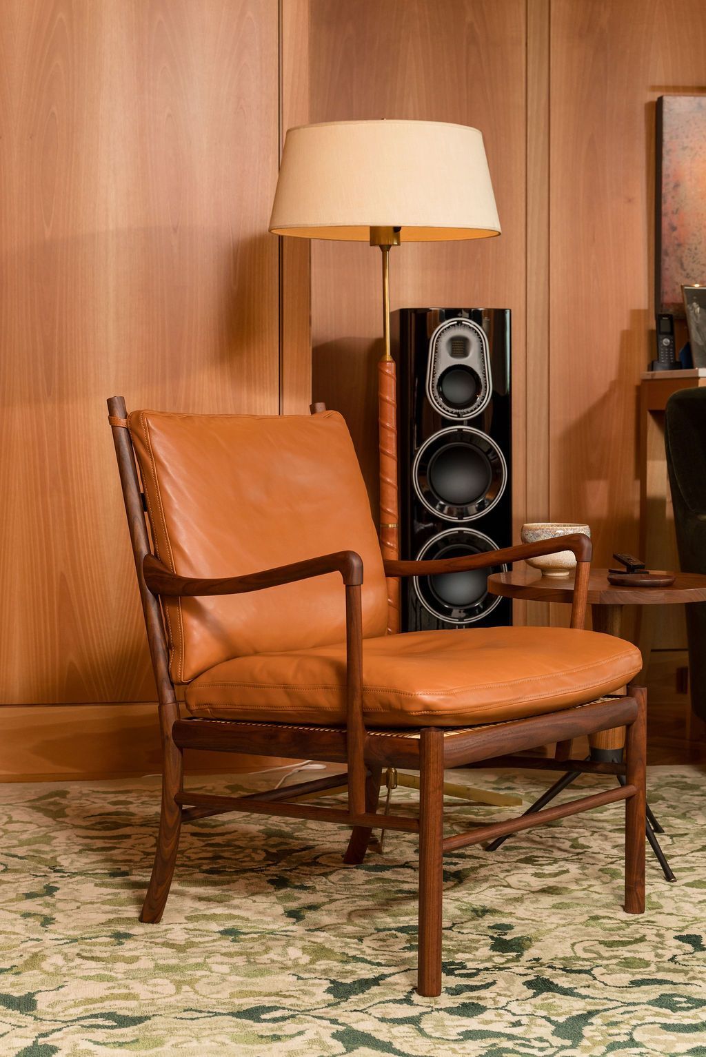 Vintage leather chair with floor lamp beside a black speaker in a wood-paneled room.