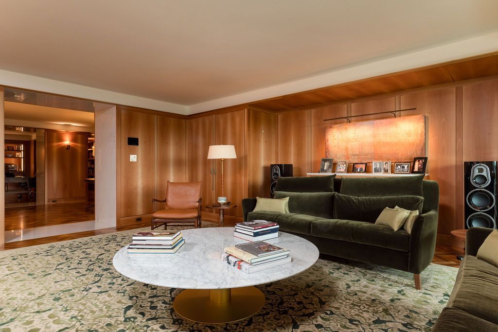 Modern living room with a round white coffee table, green sofa, wood-paneled walls, and patterned rug