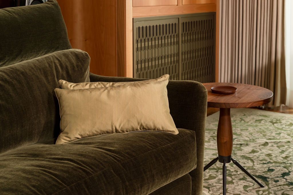 Dark green sofa with beige pillow in a cozy living room beside a round side table and patterned rug