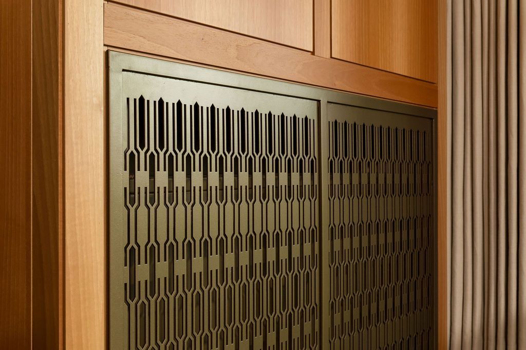 Wood-paneled wall with decorative metal grille vents in a hallway or elevator area