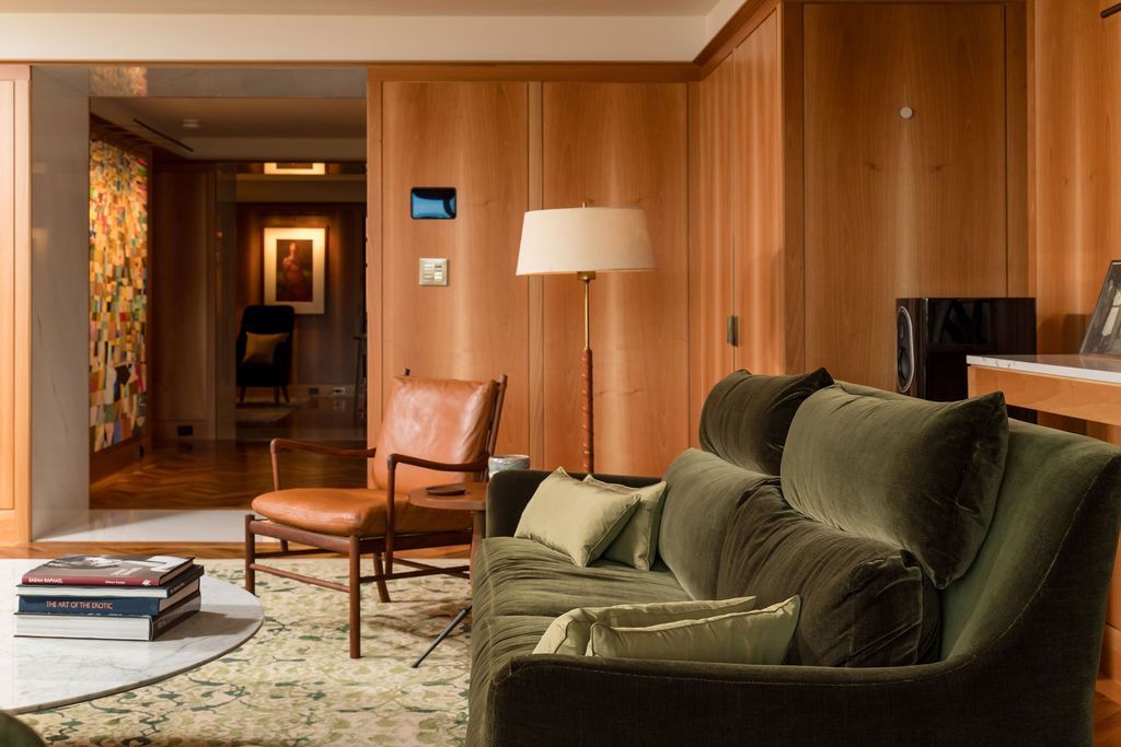 Modern living room with green sofa, leather chair, floor lamp, and wood-paneled walls