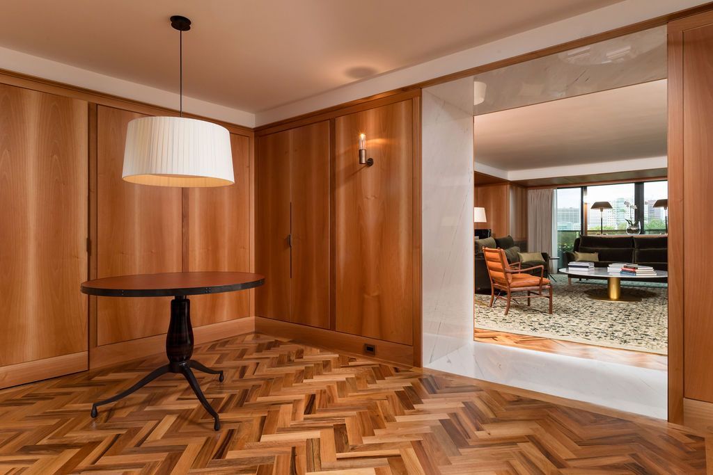 Modern wood-paneled room with a floor lamp and herringbone floor, opening to a bright dining area