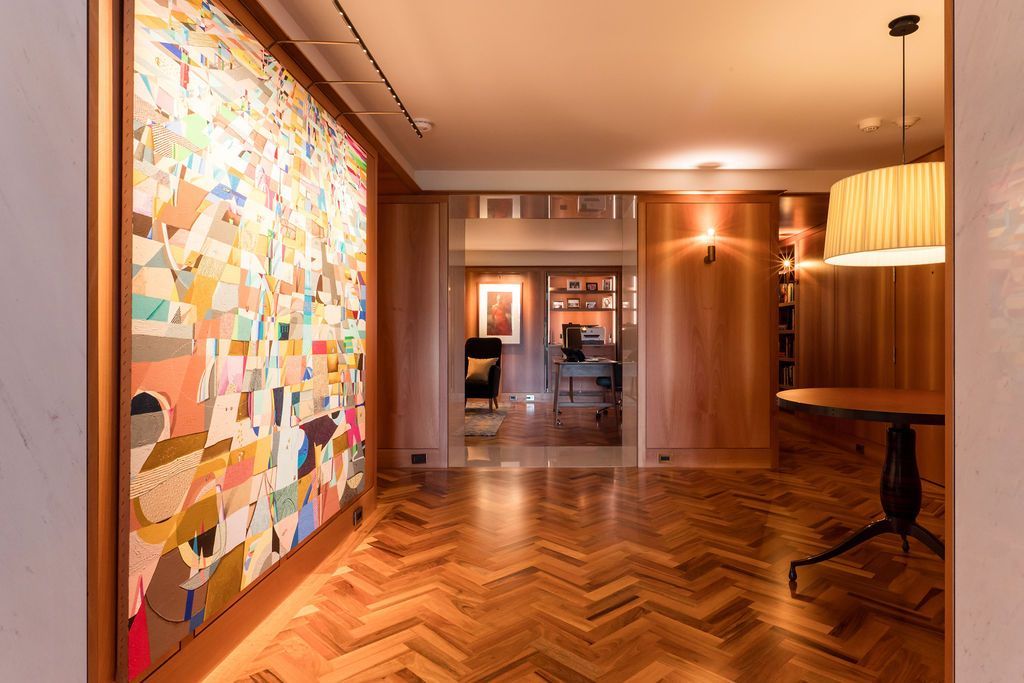Modern hallway with herringbone wood floor, colorful abstract wall art, and warm lighting