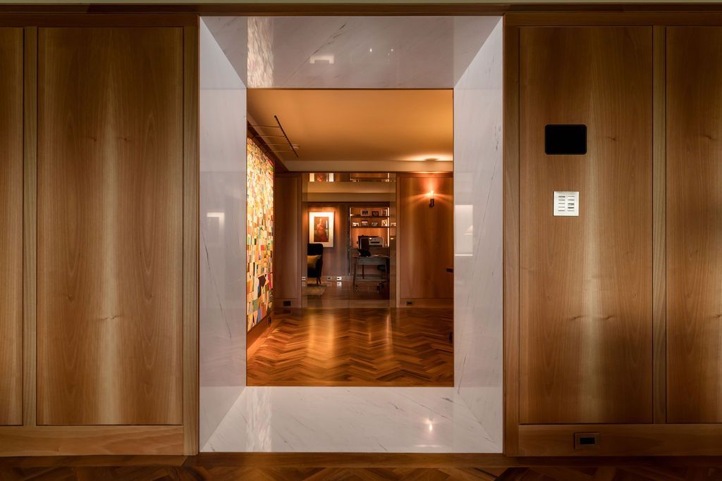 Wood-paneled hallway with a large mirror framing a warmly lit interior room beyond.