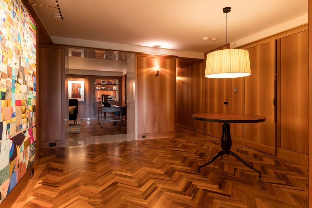 Warm wood-paneled room with herringbone floor, round table, and colorful wall art under hanging lights