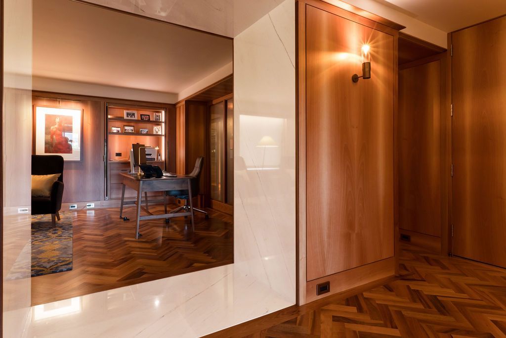 Wood-paneled hallway with herringbone floor, wall sconce, and a large mirror reflecting a dining room.