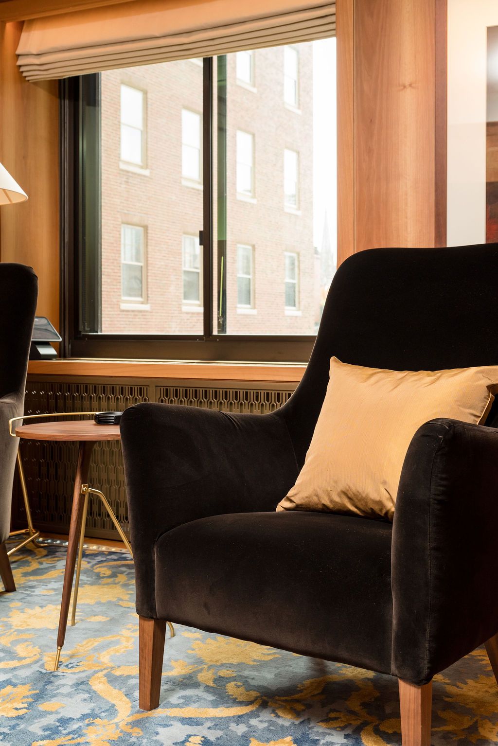 Cozy lounge with a black armchair, beige pillow, and large window beside a small table