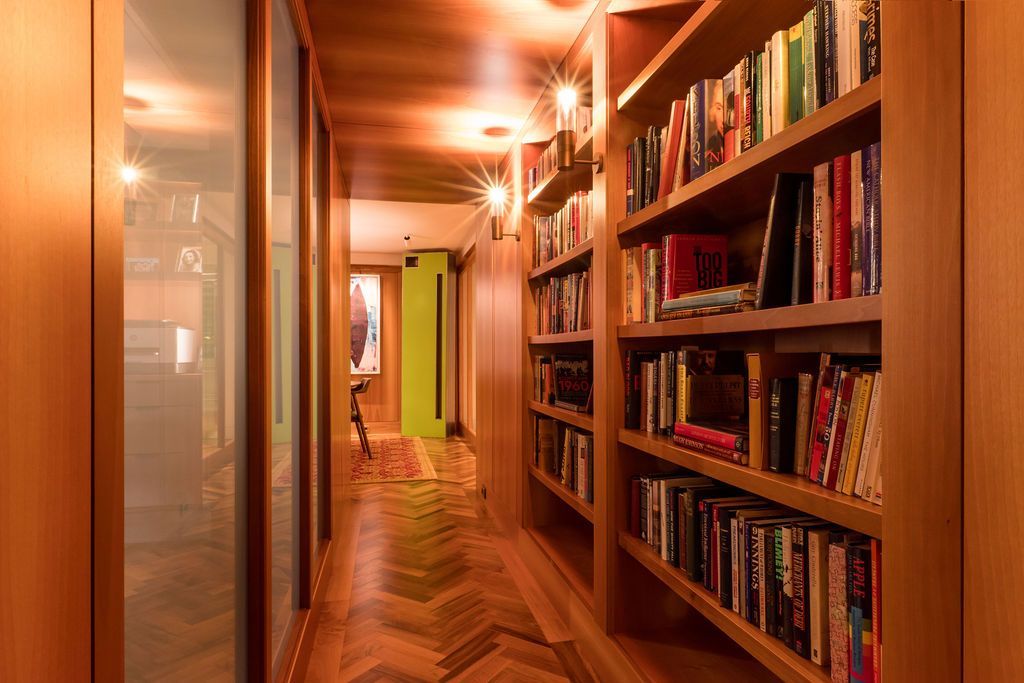 Warmly lit hallway with built-in bookshelves and wooden flooring, receding into the distance