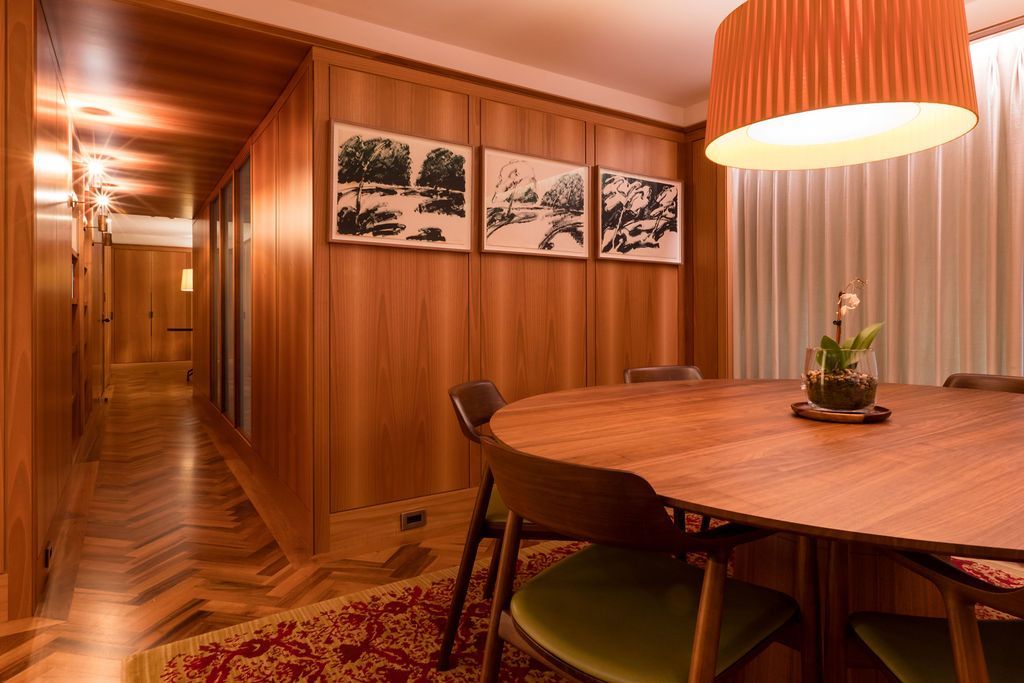 Warm wood-paneled dining room with a round table, chairs, hanging lamp, and framed wall art.