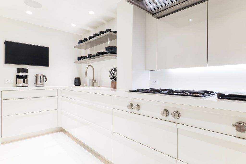 Bright white modern kitchen with black stove, wall-mounted TV, and open shelves.