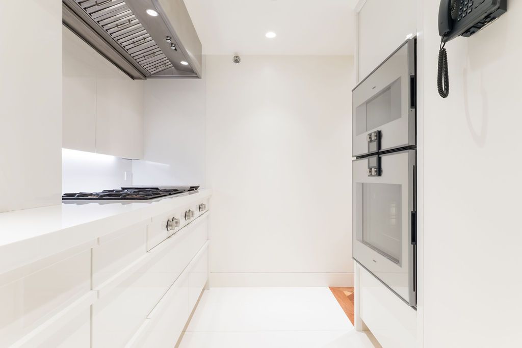 Bright white modern galley kitchen with stove, cabinets, and a wall-mounted oven