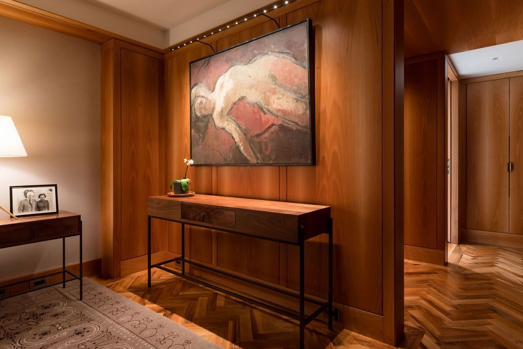 Warm wood-paneled hallway with a console table, large abstract painting, lamp, and patterned rug.
