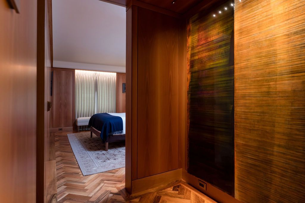 Wood-paneled hallway opening to a bedroom with a blue bed and a sunlit window.