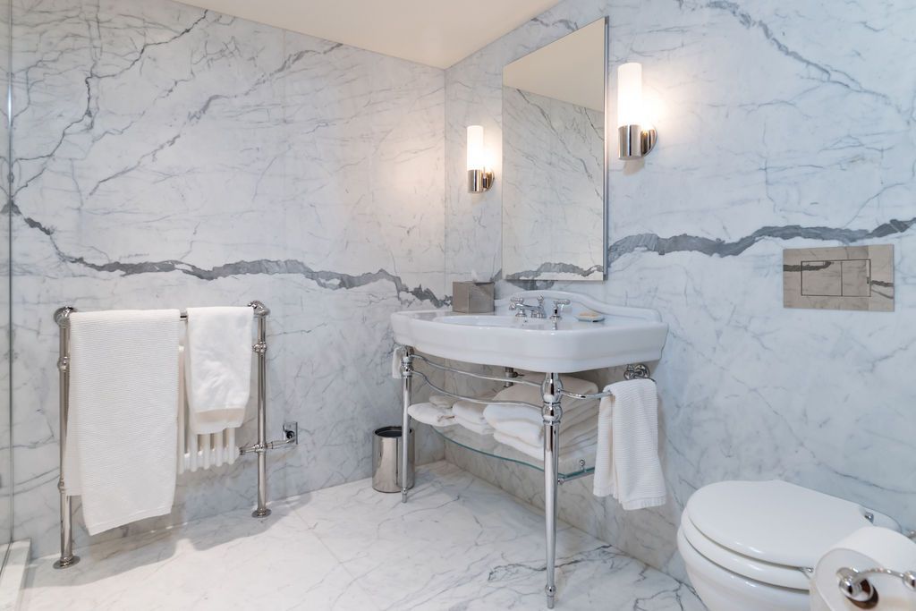 Modern marble bathroom with vanity, mirror, towel rack, and toilet