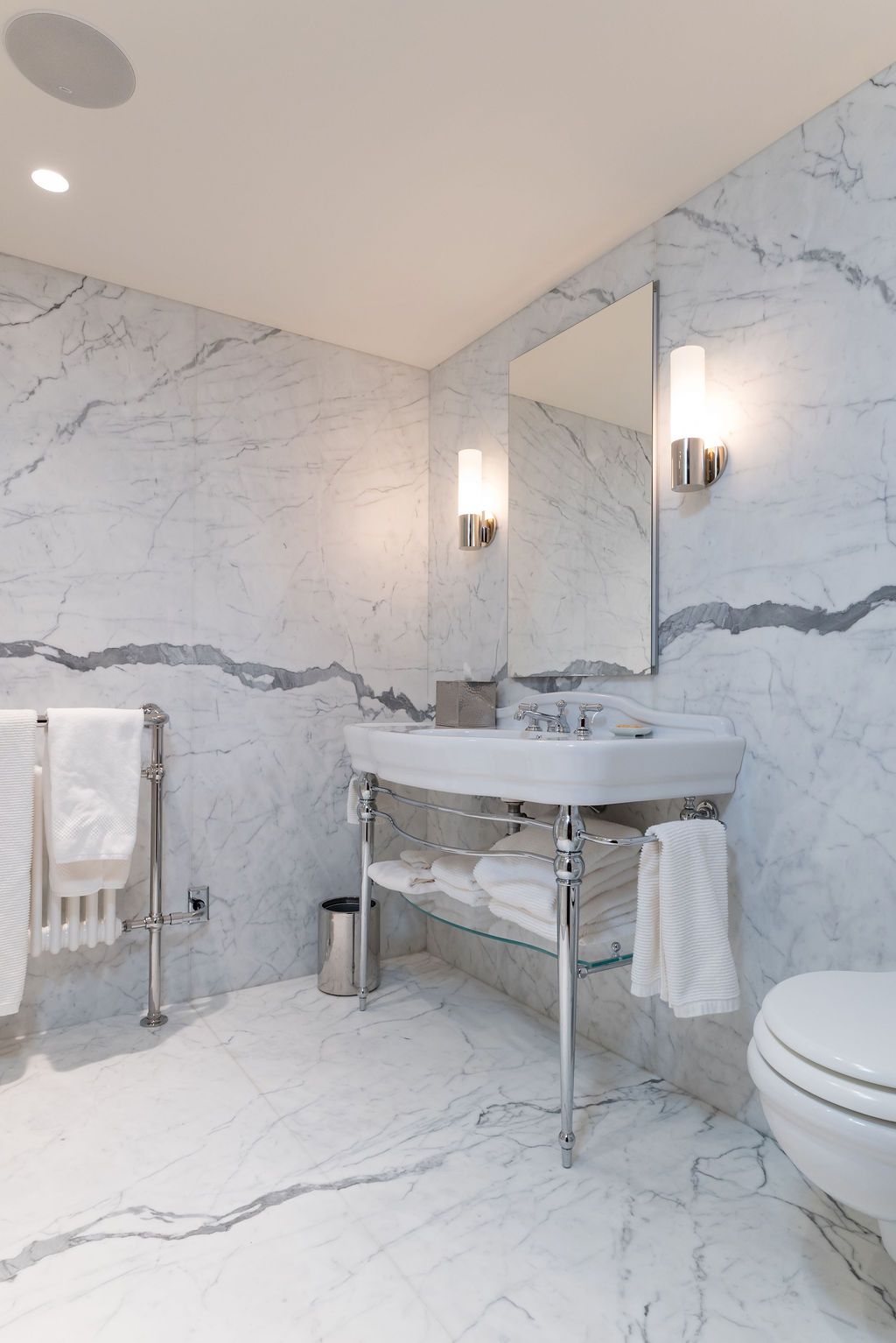 Elegant marble bathroom with pedestal sink, mirror, towel rack, and toilet