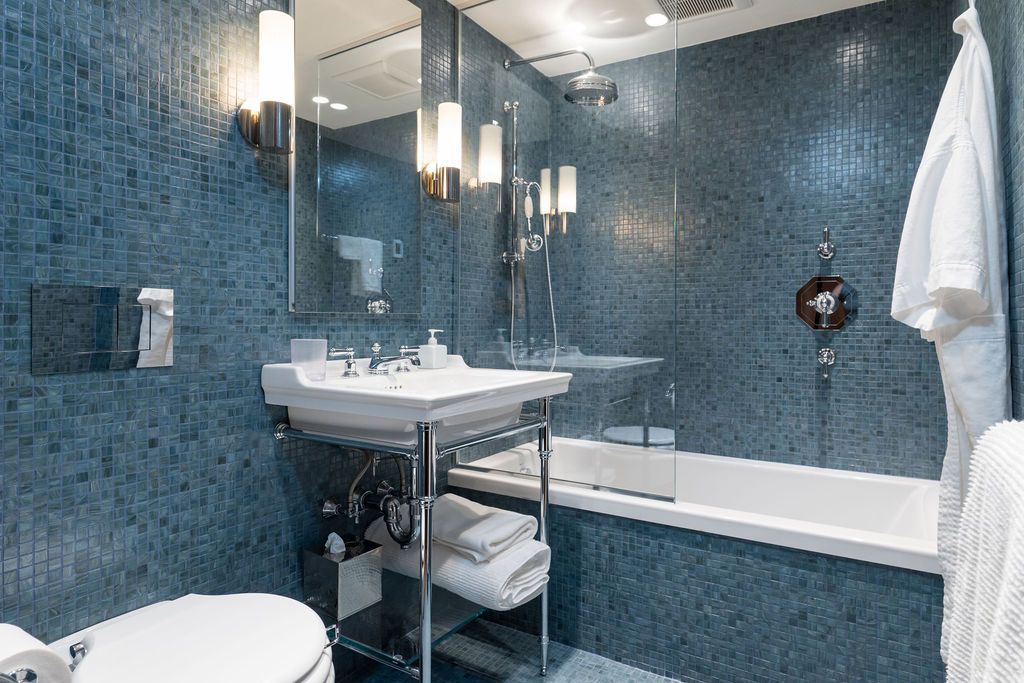 Blue-tiled bathroom with sink, mirror, bathtub, and white towel rack