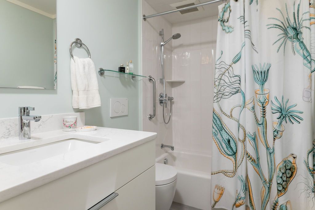 Bright bathroom with white vanity, mirror, bathtub, and teal floral shower curtain