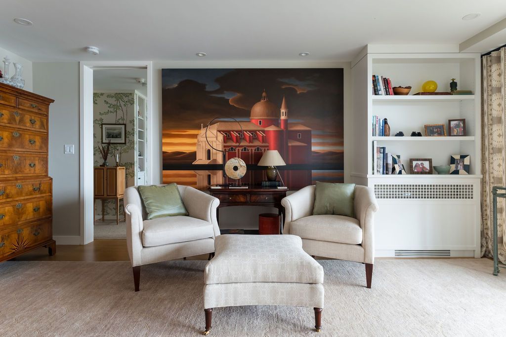Bright living room with two armchairs, ottoman, large wall art, and built-in white shelves