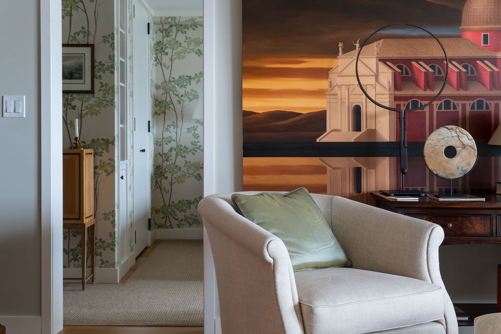 Modern living room with beige armchair, wall art, and sunset-toned mural behind an open doorway