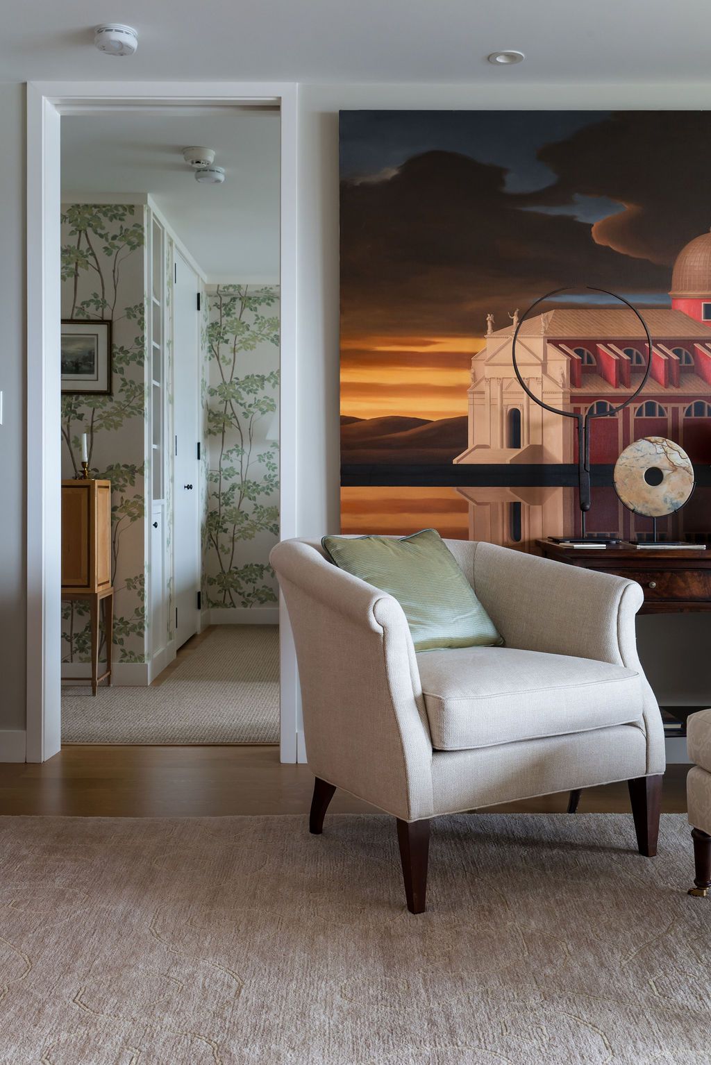 Cozy bedroom with armchair, large wall art, and an open doorway to a bright bathroom