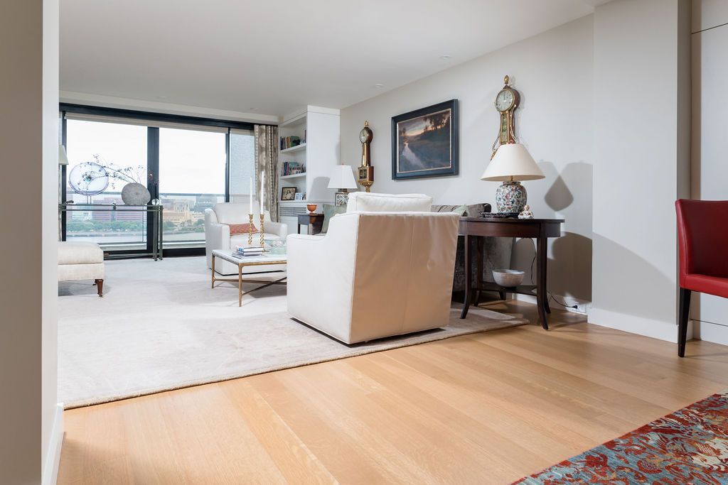 Modern living room with light wood floors, white sofa, dining table, and balcony doors