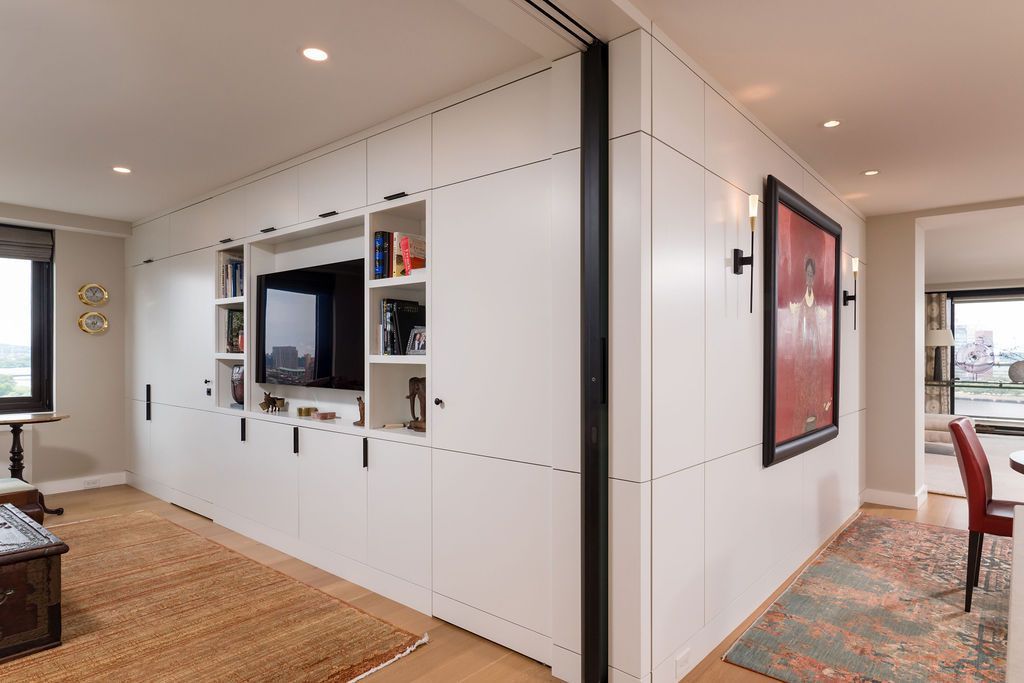Modern hallway with white paneled walls, built-in TV nook, recessed lighting, and colorful rugs