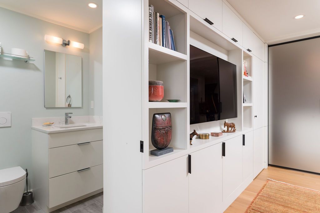 Modern living room with built-in white shelving, a TV, and a vanity area beside it