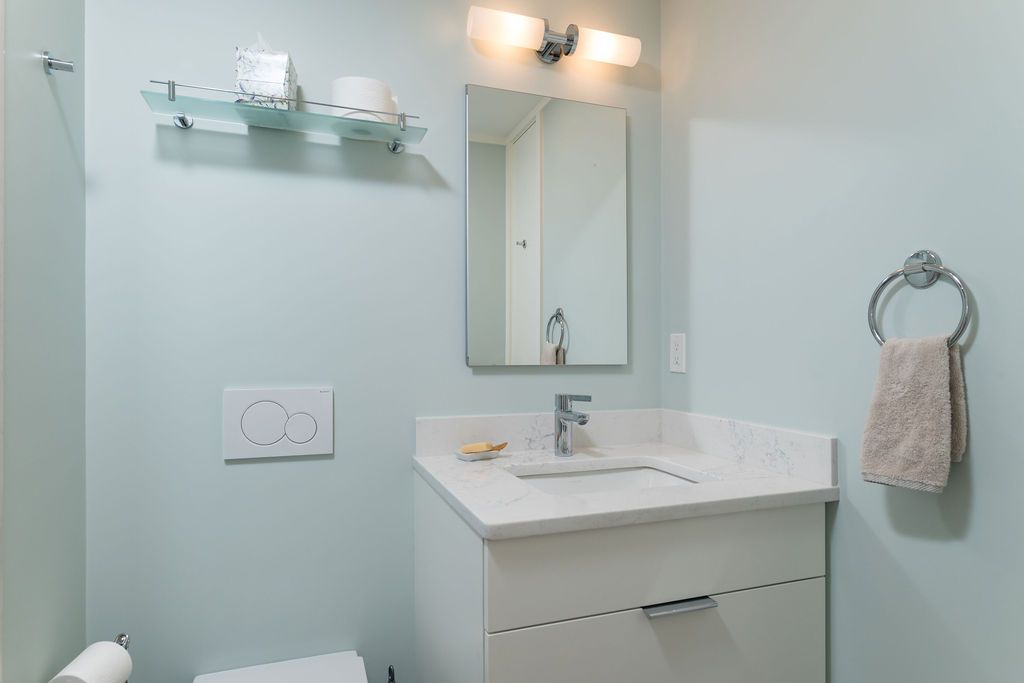 Small bathroom vanity with mirror, glass shelf, wall sconce, towel ring, and pale blue walls