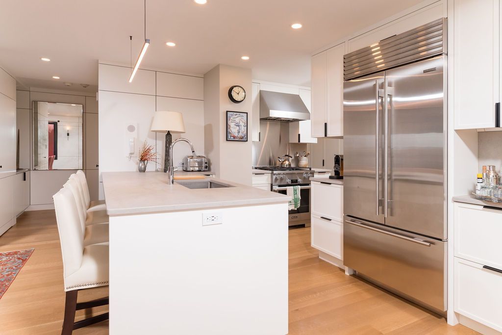 Modern white kitchen with stainless steel appliances, island seating, and light wood floors