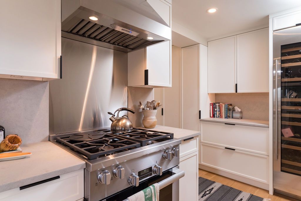 Modern kitchen with stainless steel stove, white cabinets, and a marble backsplash