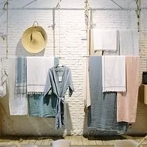 Display of towels and a bathrobe in a shop. Beige brick wall with hanging garments in various pastel colors.