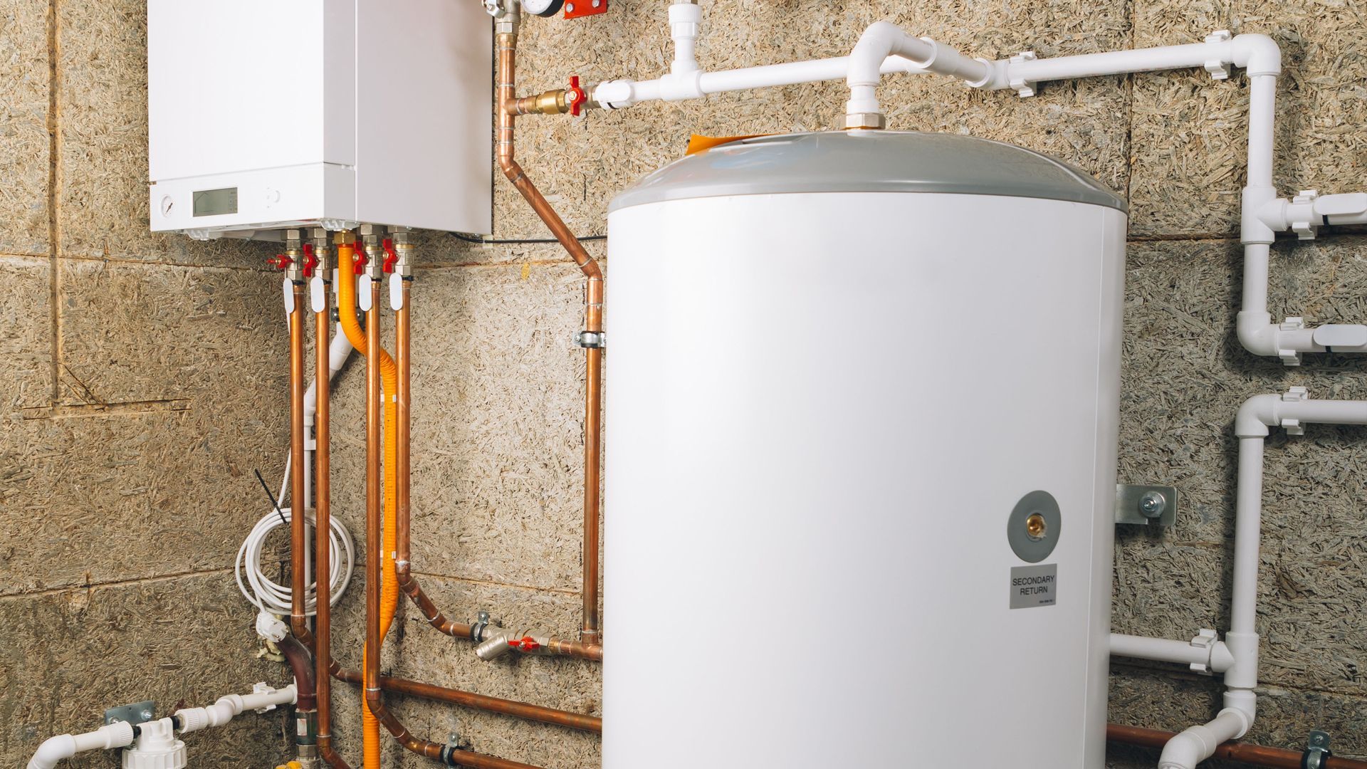 Water heater and boiler unit with exposed copper and white pipes in a utility room