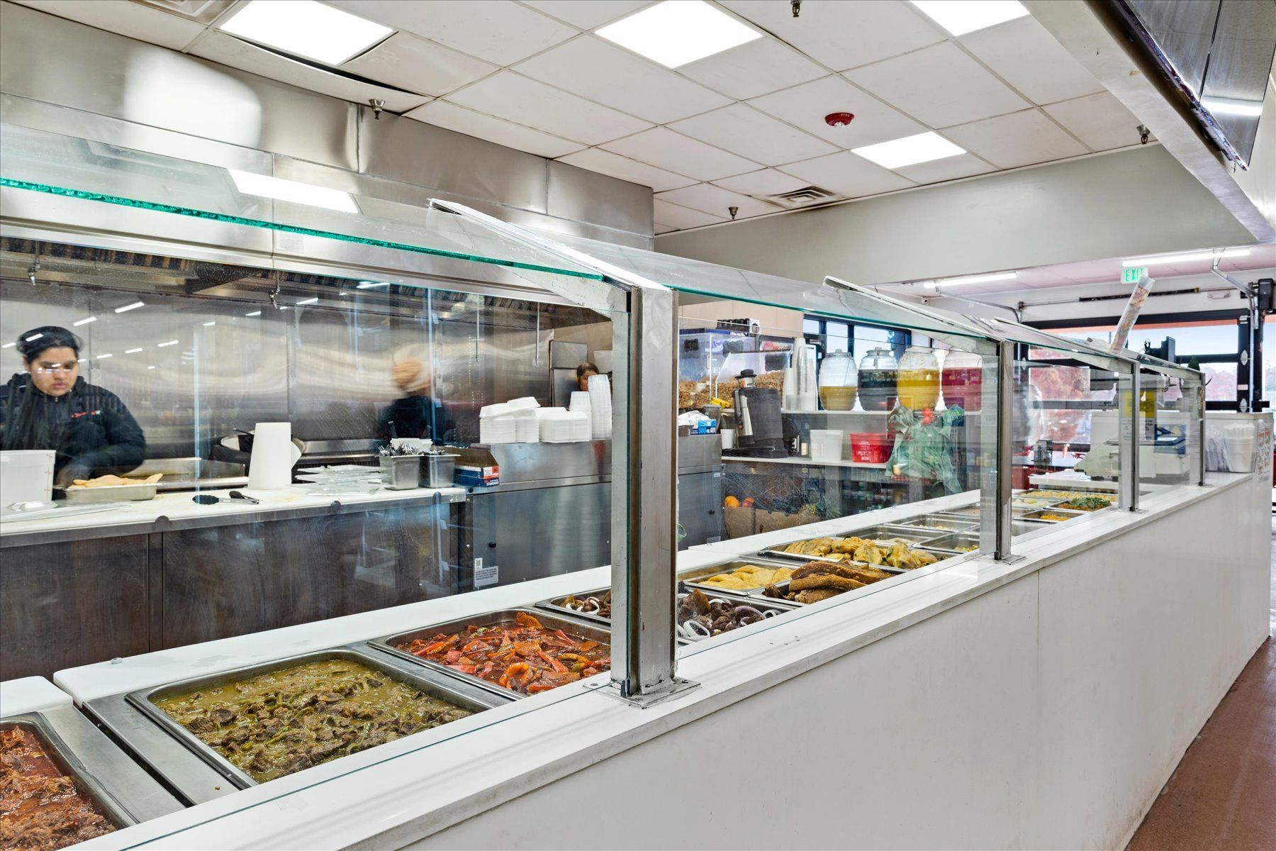 A woman is preparing food in a buffet line in a restaurant.