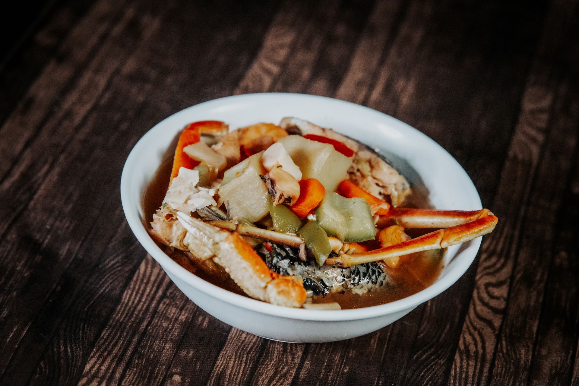A bowl of soup with crab and vegetables on a wooden table.