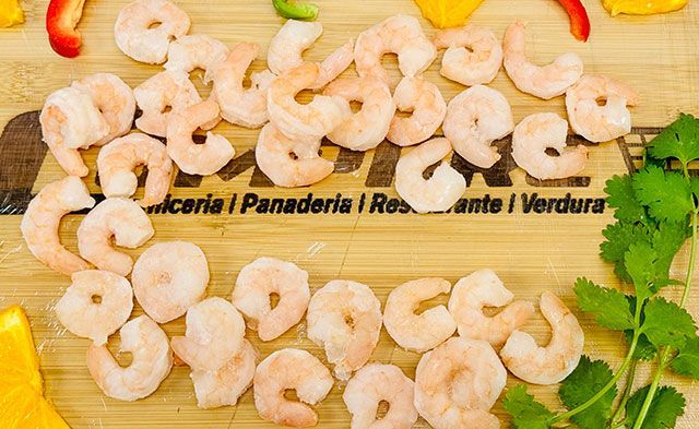 A bunch of shrimp are sitting on top of a wooden cutting board