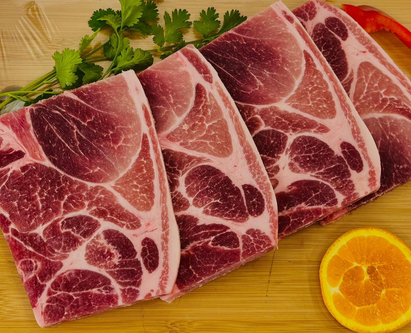 A piece of meat is sitting on a wooden table next to an orange slice