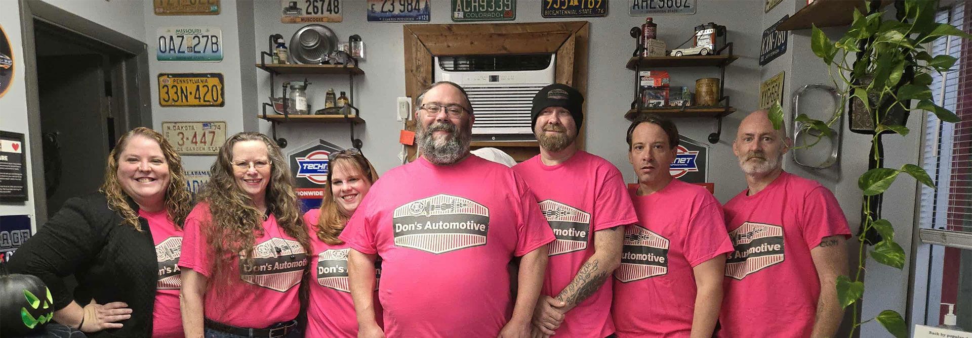 Group of people wearing pink t-shirts posing in a shop with license plates on the wall.