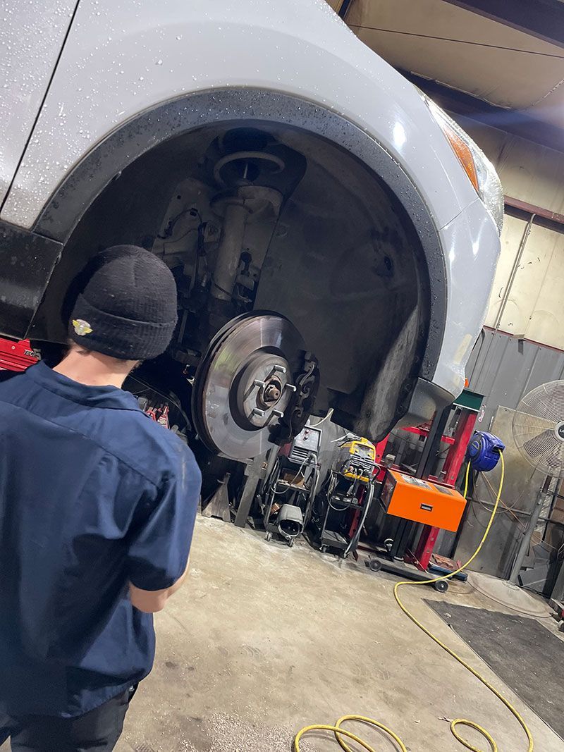 Mechanic working on the brake system of a white car, raised on a lift, inside a garage.