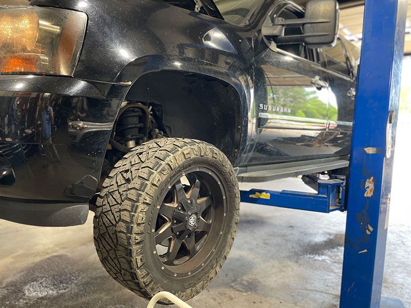 Black truck on a lift with a tire removed, in a repair shop.