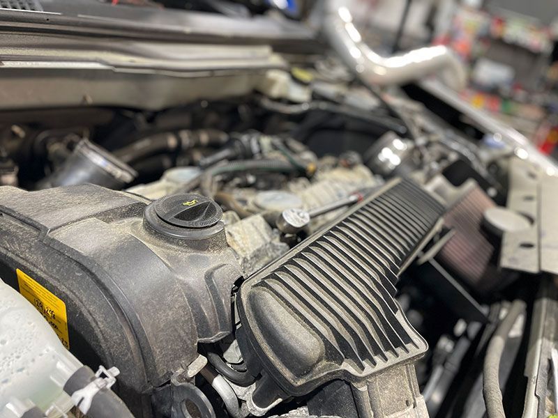 Car engine bay with air intake system visible. Dusty, gray engine components.