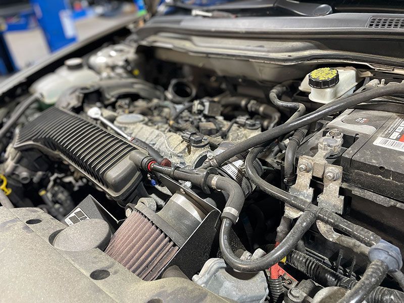 Engine bay of a car with an aftermarket air intake, various hoses, and battery.