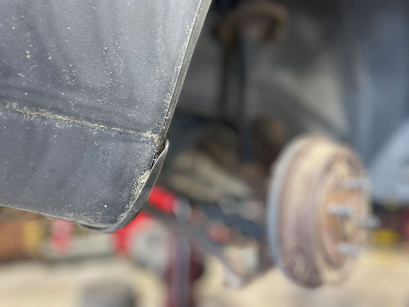 Close-up of a black car's fender with a rusty brake drum and suspension components in the blurry background.